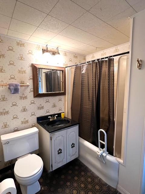 full bath with wallpapered walls, shower / bath combo, vanity, and toilet
