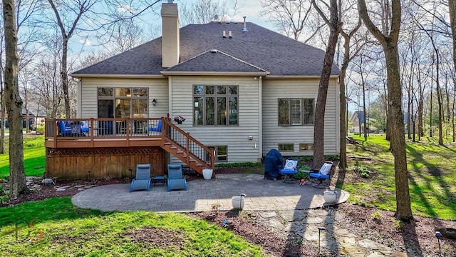rear view of property featuring roof with shingles, a chimney, a wooden deck, stairway, and a patio