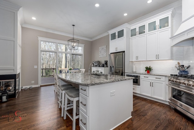 kitchen featuring wall chimney range hood, ornamental molding, an island with sink, and stainless steel appliances