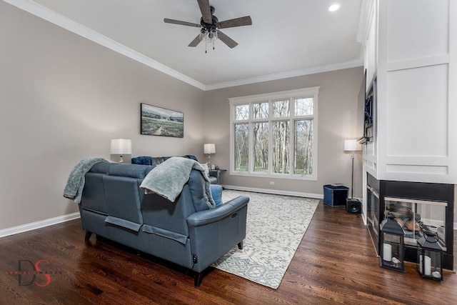 living room featuring a ceiling fan, crown molding, a multi sided fireplace, baseboards, and dark wood-style floors