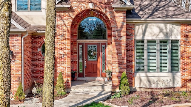 doorway to property with a shingled roof and brick siding