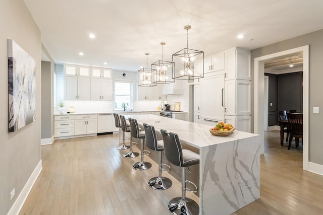 kitchen with light wood-type flooring, dishwasher, backsplash, white cabinets, and baseboards