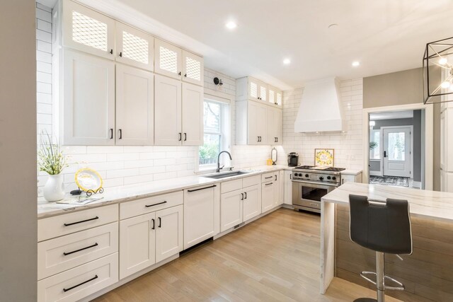 kitchen featuring white dishwasher, stainless steel range, a sink, wall chimney range hood, and tasteful backsplash