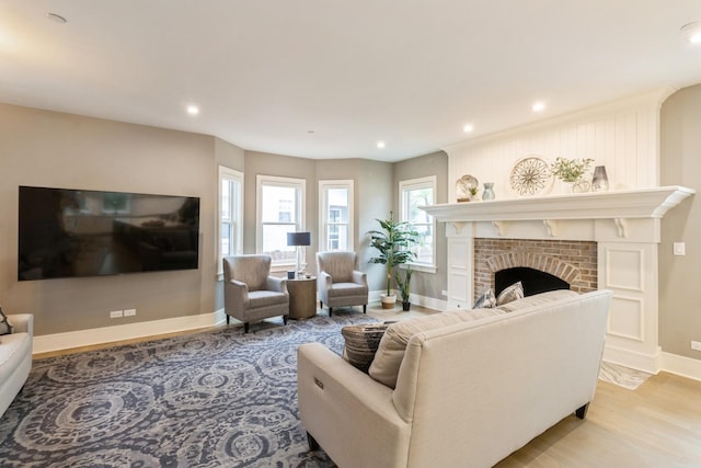 living area with light wood-style flooring, baseboards, a brick fireplace, and recessed lighting