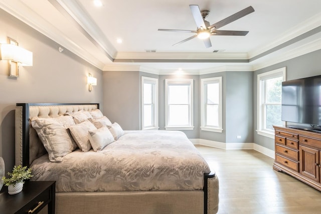 bedroom with a ceiling fan, light wood-style flooring, baseboards, crown molding, and a raised ceiling