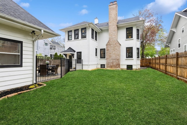 rear view of property featuring a chimney, a yard, a shingled roof, and a fenced backyard