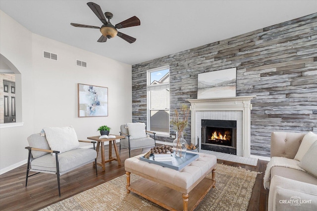 living room with wood finished floors, visible vents, a ceiling fan, arched walkways, and a fireplace