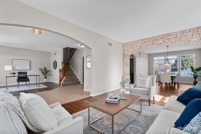 living area featuring arched walkways, baseboards, visible vents, wood finished floors, and stairs