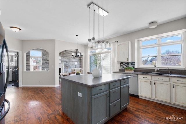 kitchen with stainless steel dishwasher, dark countertops, a sink, dark wood finished floors, and a notable chandelier