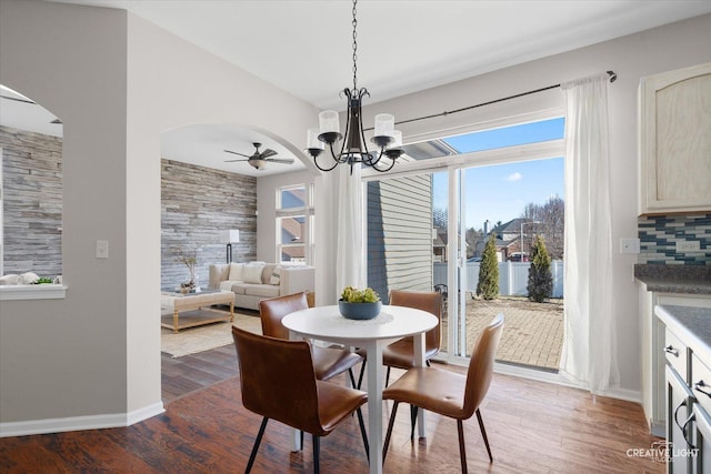 dining room featuring ceiling fan with notable chandelier, baseboards, wood finished floors, and arched walkways
