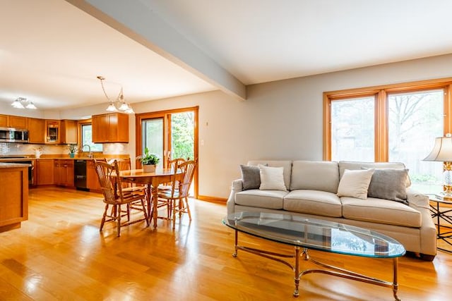 living area with beamed ceiling, baseboards, and light wood-style flooring