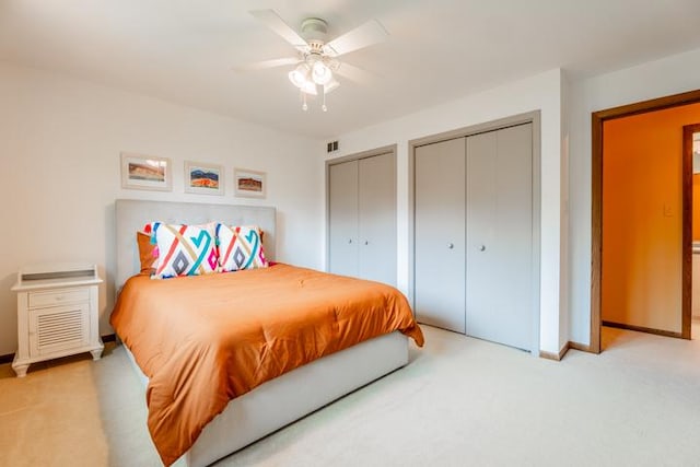 bedroom featuring a ceiling fan, visible vents, baseboards, two closets, and light carpet