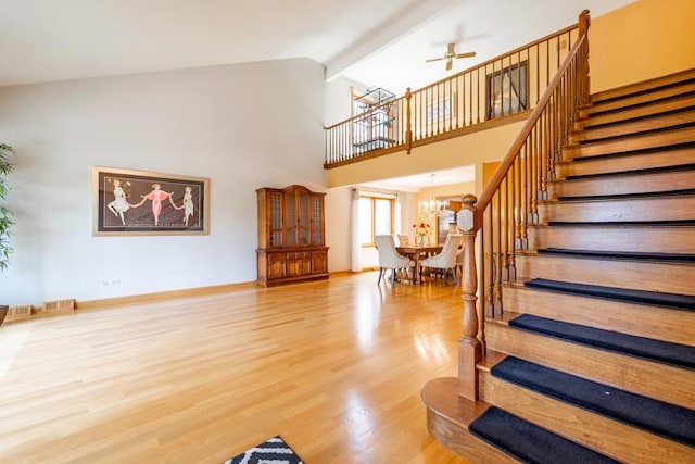 staircase featuring high vaulted ceiling, ceiling fan with notable chandelier, and wood finished floors