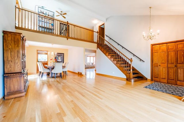 foyer entrance featuring light wood-type flooring, high vaulted ceiling, baseboards, ceiling fan with notable chandelier, and stairs