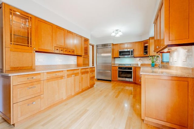 kitchen featuring light wood-style floors, brown cabinets, light stone counters, a sink, and appliances with stainless steel finishes