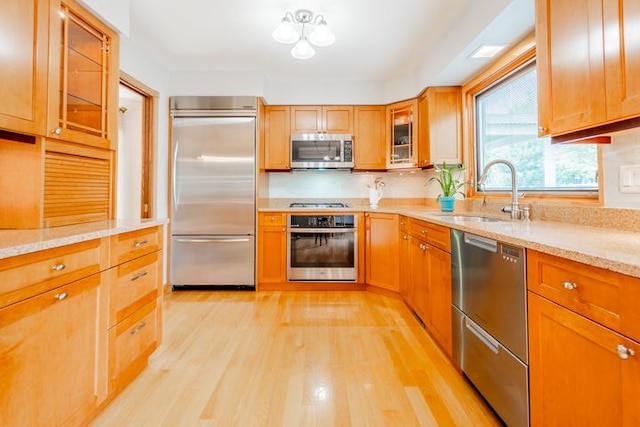 kitchen with light stone countertops, glass insert cabinets, light wood-style floors, a sink, and appliances with stainless steel finishes