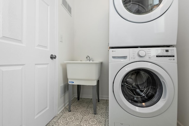 laundry area with stacked washer and clothes dryer, light tile patterned floors, and baseboards