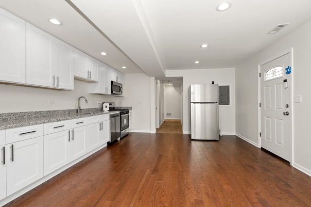 kitchen featuring stainless steel appliances, white cabinetry, light stone countertops, dark wood finished floors, and a sink