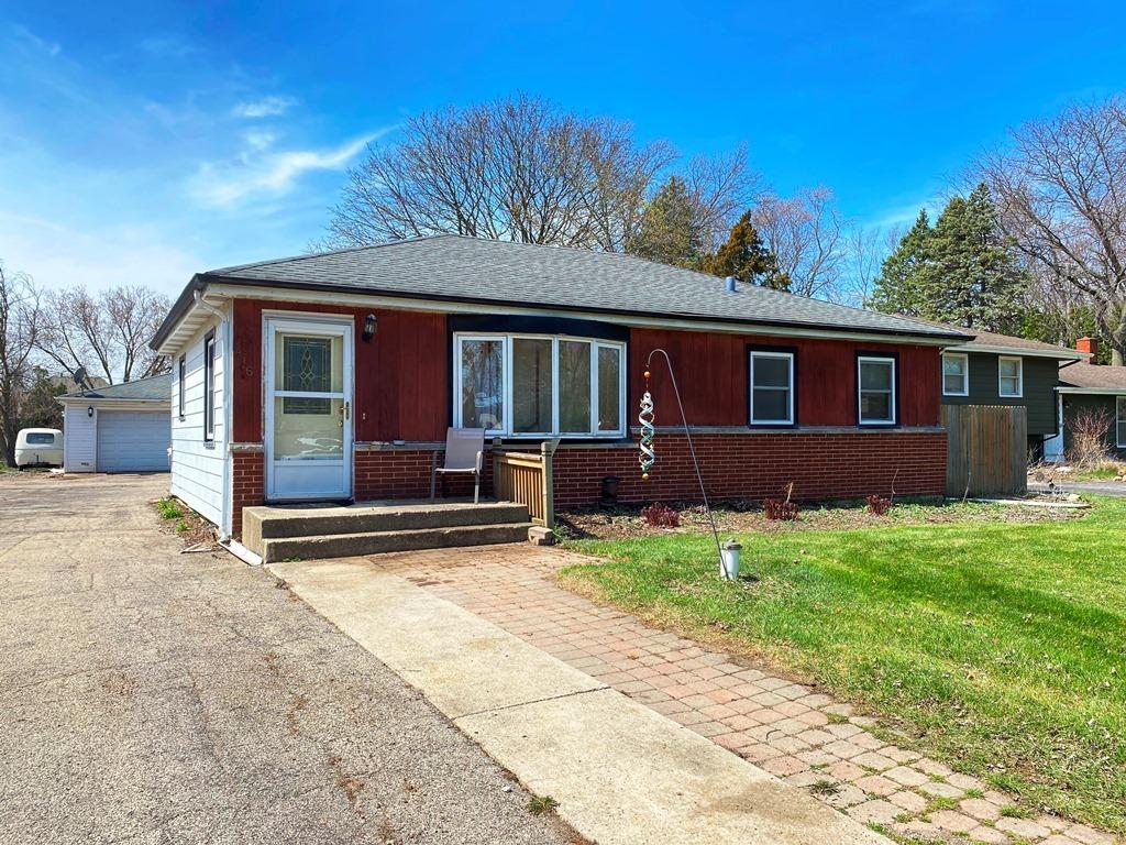 view of front of house featuring a detached garage, a shingled roof, a front lawn, and brick siding
