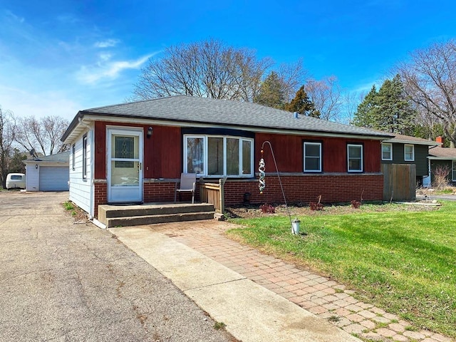 view of front of house featuring a detached garage, a shingled roof, a front lawn, and brick siding