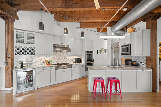 kitchen featuring a sink, beverage cooler, built in appliances, wood ceiling, and under cabinet range hood