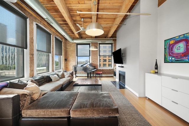 living room featuring a fireplace with flush hearth, beamed ceiling, light wood-type flooring, wood ceiling, and brick wall