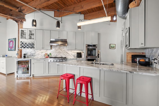 kitchen with beverage cooler, under cabinet range hood, stainless steel appliances, a sink, and a peninsula