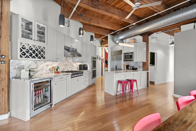 kitchen with tasteful backsplash, a sink, beverage cooler, built in appliances, and under cabinet range hood