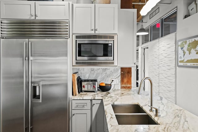 kitchen featuring a sink, white cabinetry, backsplash, built in appliances, and light stone counters