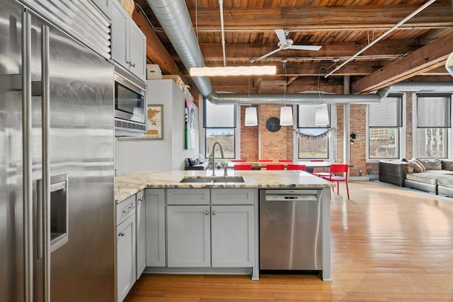 kitchen with a sink, light wood-type flooring, built in appliances, brick wall, and wooden ceiling