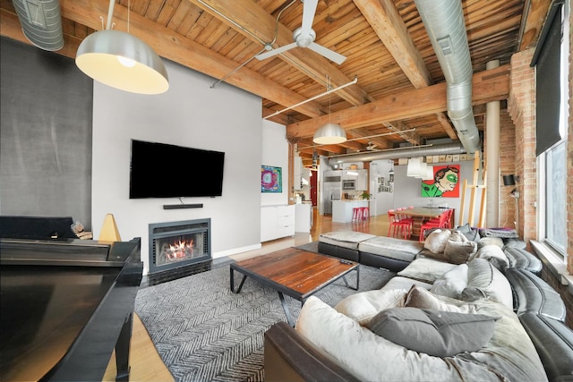 living area with wood finished floors, wood ceiling, ceiling fan, a lit fireplace, and beamed ceiling