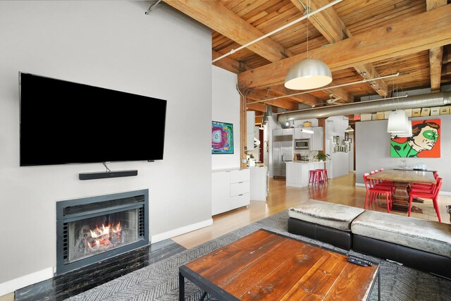 living area featuring a warm lit fireplace, wood ceiling, beamed ceiling, light wood finished floors, and baseboards