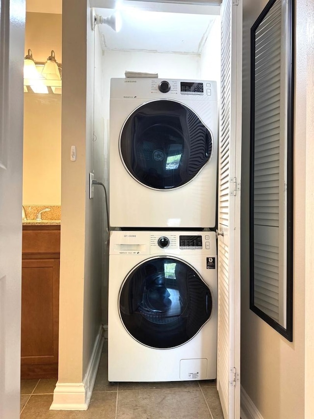 laundry room with stacked washer / dryer, light tile patterned flooring, and baseboards