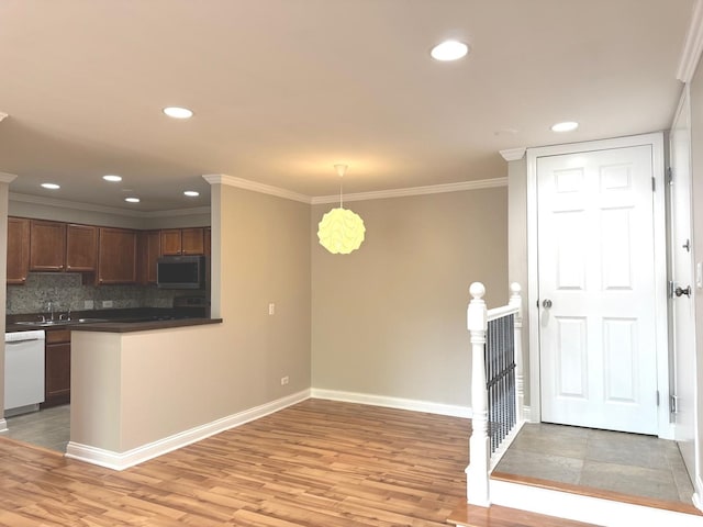 kitchen featuring stainless steel microwave, dishwasher, light wood finished floors, dark countertops, and baseboards
