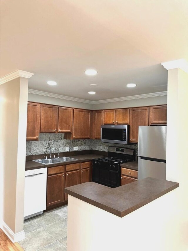 kitchen with stainless steel appliances, a sink, dark countertops, decorative backsplash, and brown cabinetry