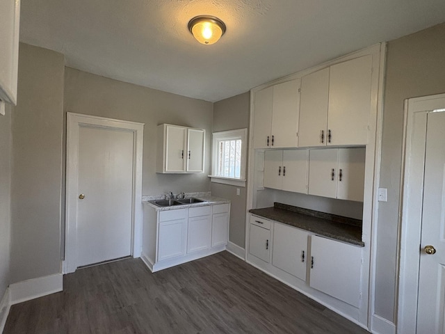 kitchen featuring white cabinets, baseboards, dark wood-style floors, and a sink