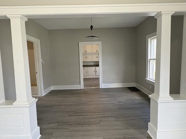 unfurnished dining area with baseboards, dark wood-style floors, and decorative columns