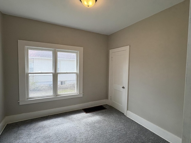 empty room featuring visible vents, baseboards, and dark carpet