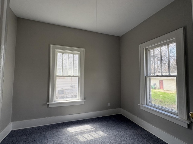 spare room featuring dark carpet, baseboards, and a healthy amount of sunlight