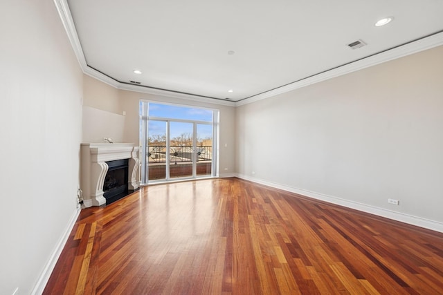 unfurnished living room with wood finished floors, visible vents, a fireplace, and crown molding