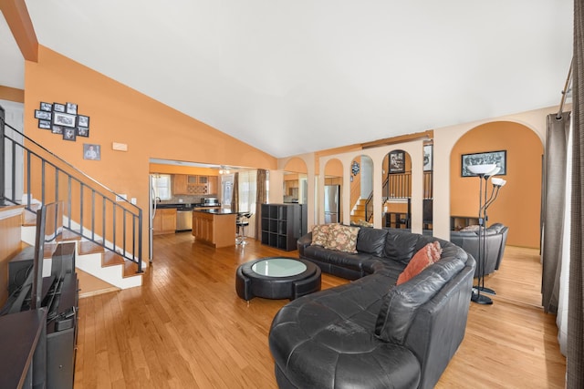 living area featuring high vaulted ceiling, arched walkways, light wood finished floors, and stairs