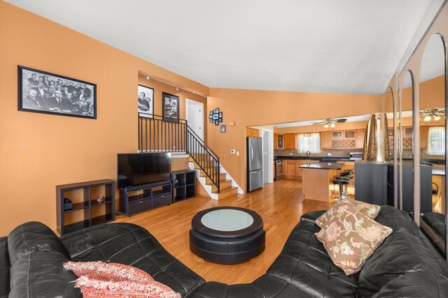 living room featuring light wood-type flooring, a ceiling fan, and stairway