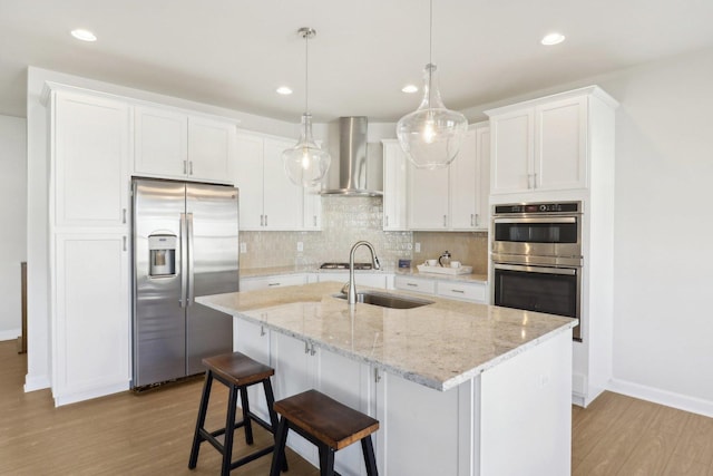 kitchen featuring wood finished floors, a sink, wall chimney exhaust hood, baseboards, and appliances with stainless steel finishes