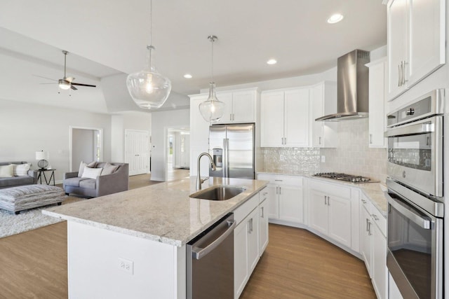 kitchen with wood finished floors, wall chimney exhaust hood, stainless steel appliances, and a sink