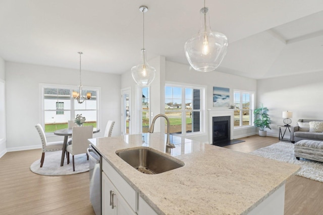 kitchen featuring light wood finished floors, stainless steel dishwasher, a sink, open floor plan, and a fireplace with raised hearth