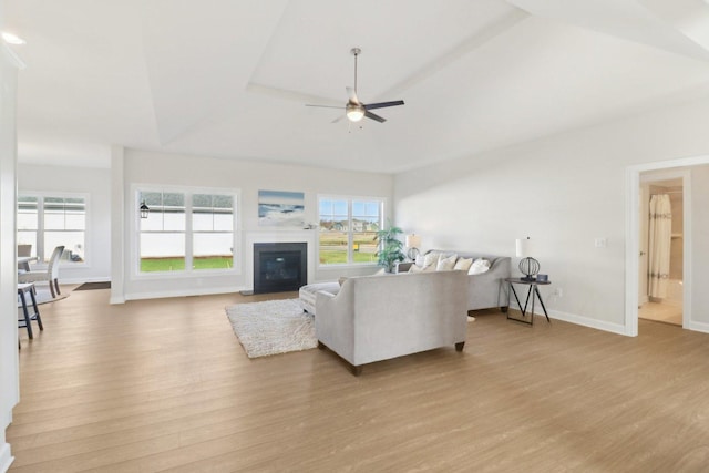 living area featuring a glass covered fireplace, light wood-style flooring, a ceiling fan, and baseboards