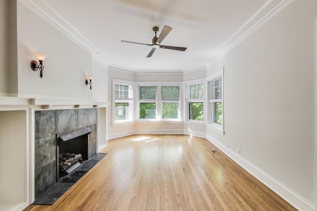 unfurnished living room featuring hardwood / wood-style floors, crown molding, a premium fireplace, baseboards, and a ceiling fan
