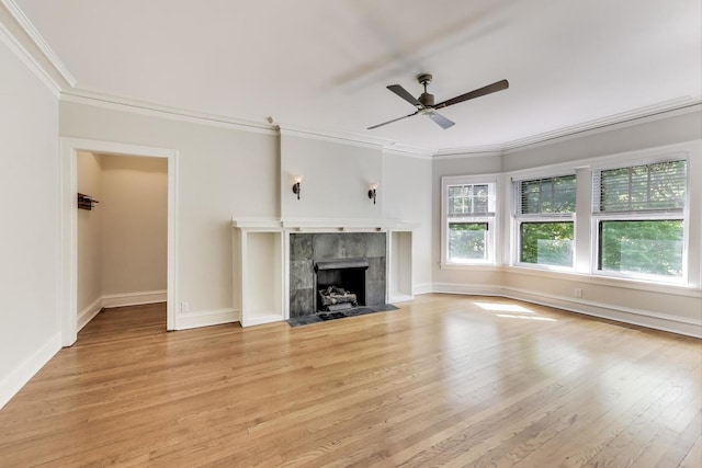 unfurnished living room with ornamental molding, ceiling fan, light wood finished floors, a tiled fireplace, and baseboards