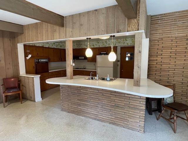 kitchen featuring beam ceiling, wood walls, freestanding refrigerator, wall oven, and range hood