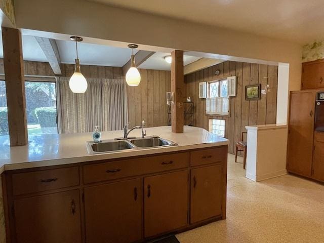 kitchen with decorative light fixtures, wood walls, a sink, light countertops, and beamed ceiling